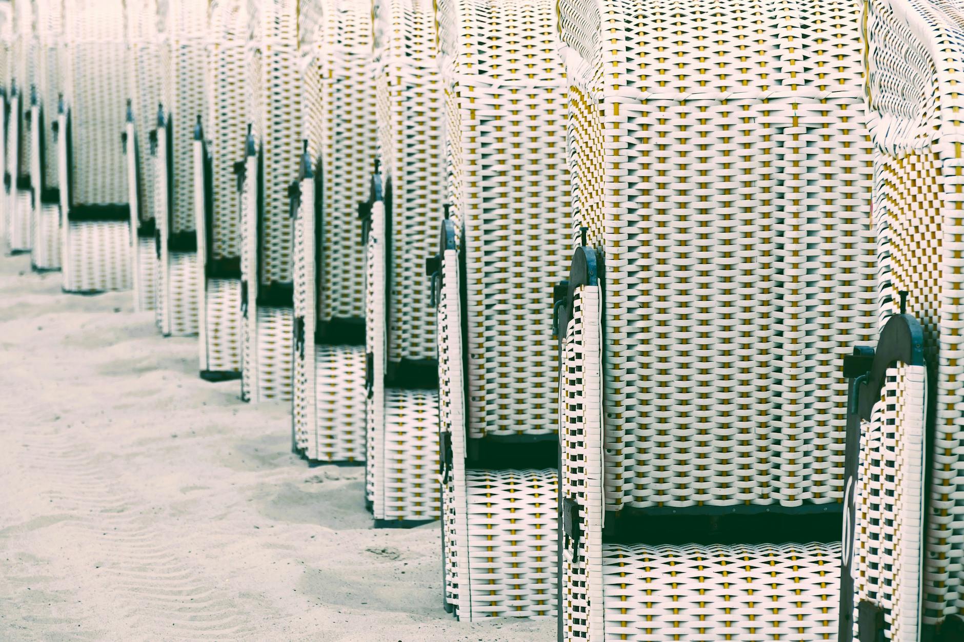 A line of wicker beach chairs arranged neatly on a sandy shoreline, capturing a serene coastal scene.
