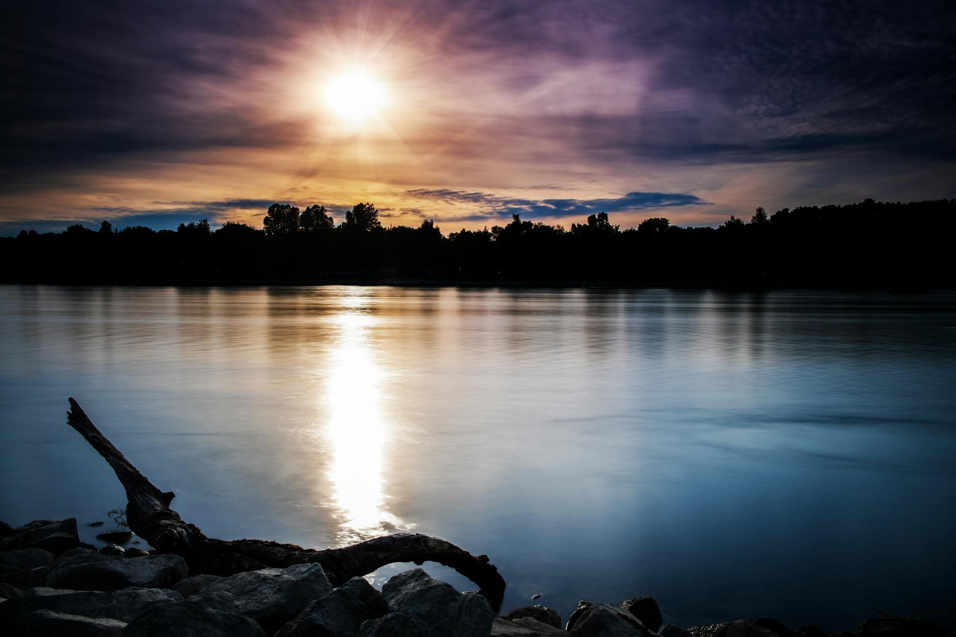 Tranquil sunset over a calm river in Speyer, Germany, casting reflections on the water.