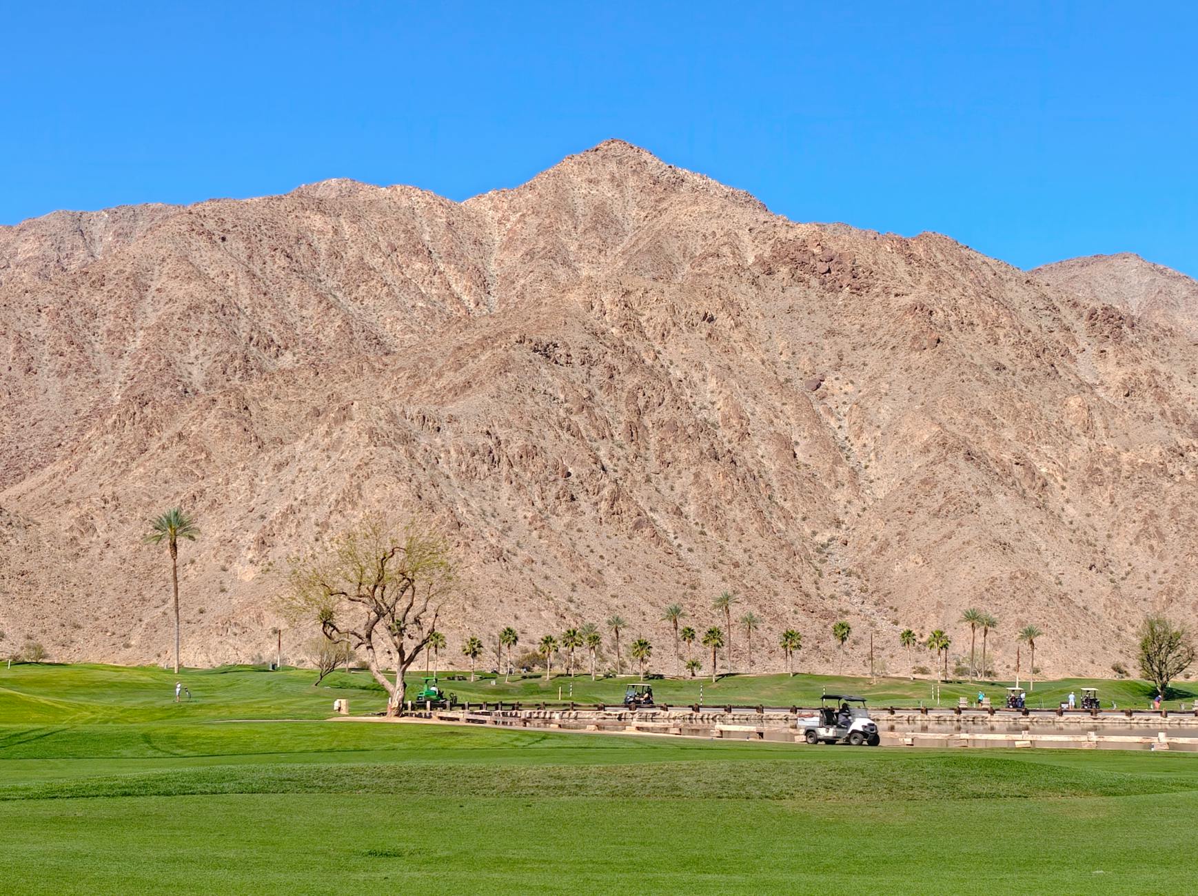 Beautiful view of a golf course with mountains in Indian Wells, CA under a clear blue sky.