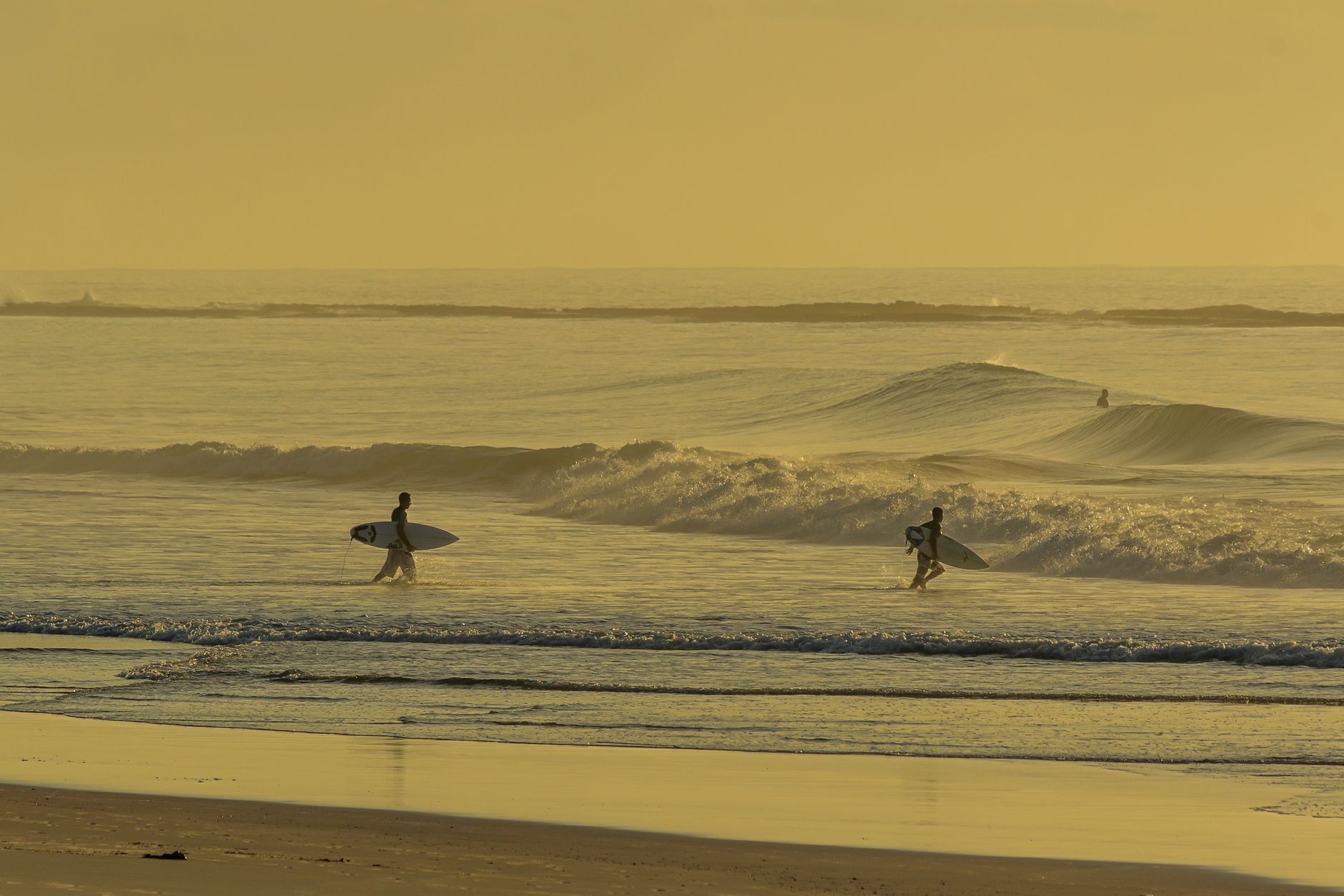 Two surfers head towards the waves in a serene sunset beach setting. Perfect for ocean lovers.