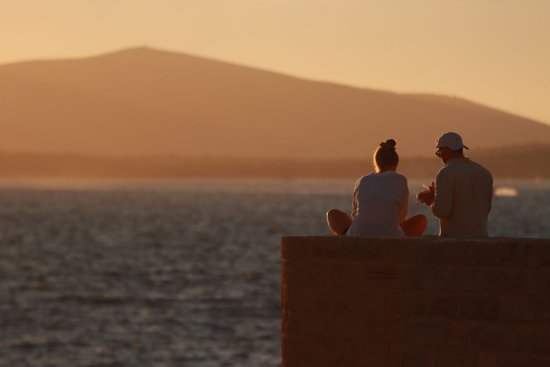 Couple enjoying a serene sunset by the shore in Alghero, Sardinia, Italy.