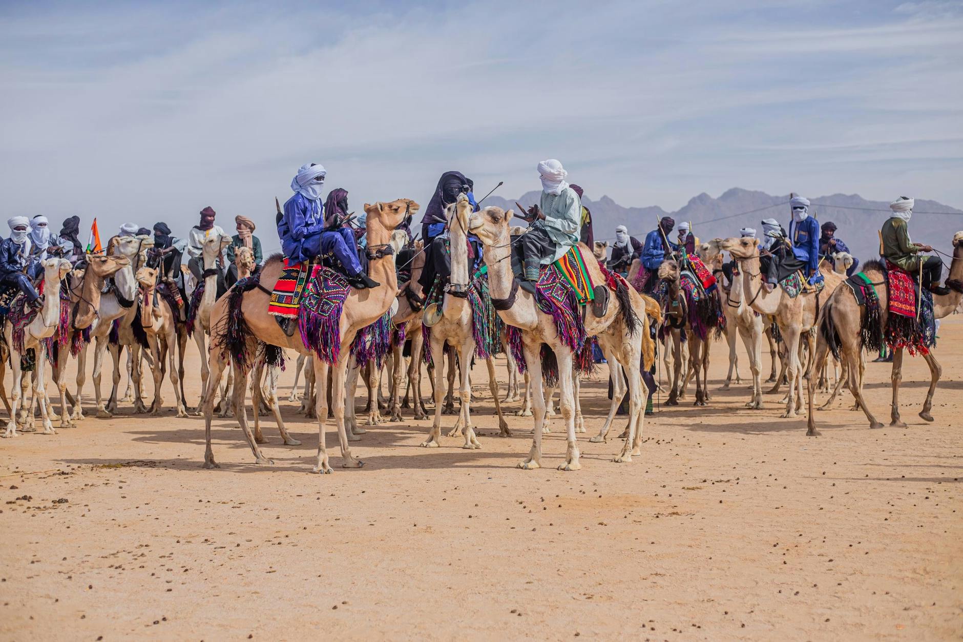 Nomads on camels traverse a vast desert, showcasing cultural heritage and traditional attire.
