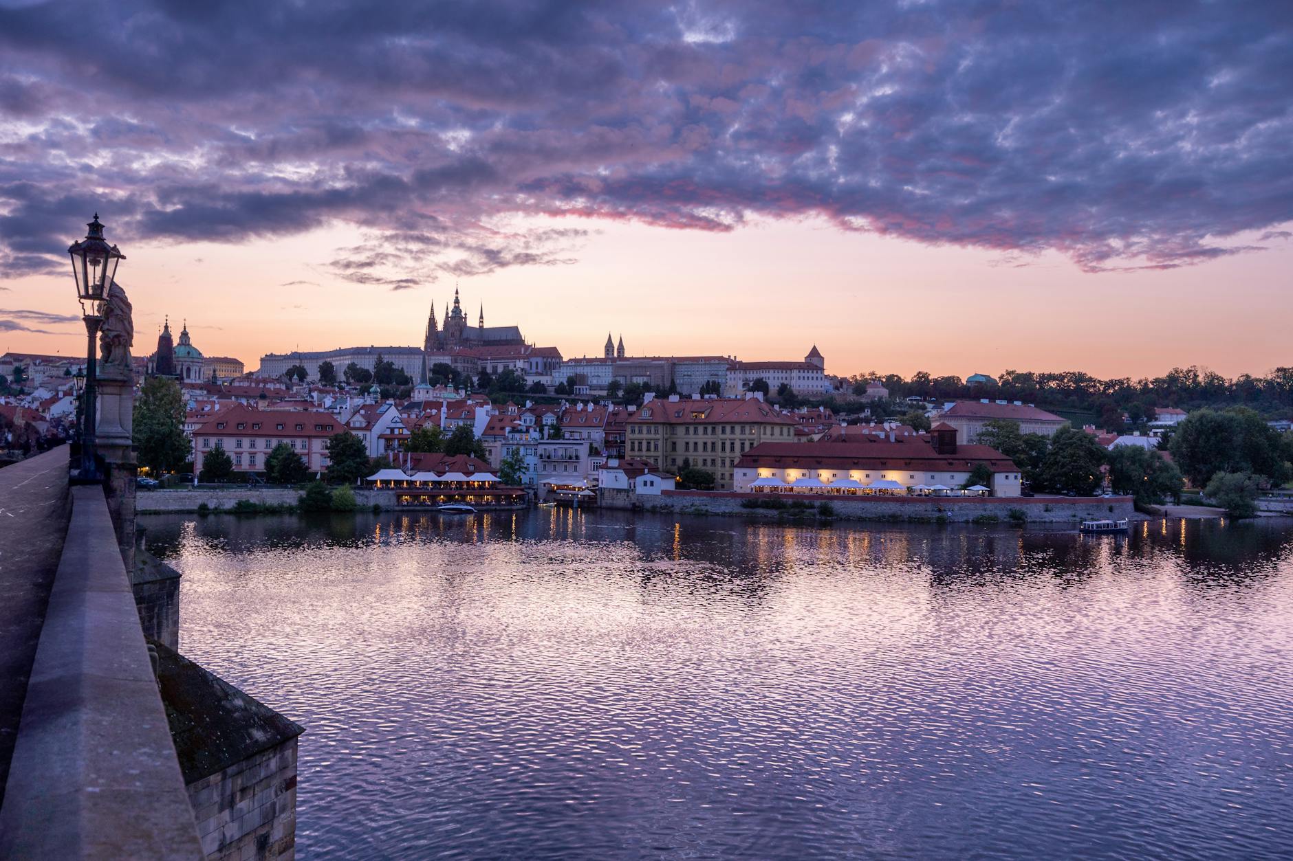Stunning view of Prague Castle from Charles Bridge during sunset, reflecting in the Vltava River.
