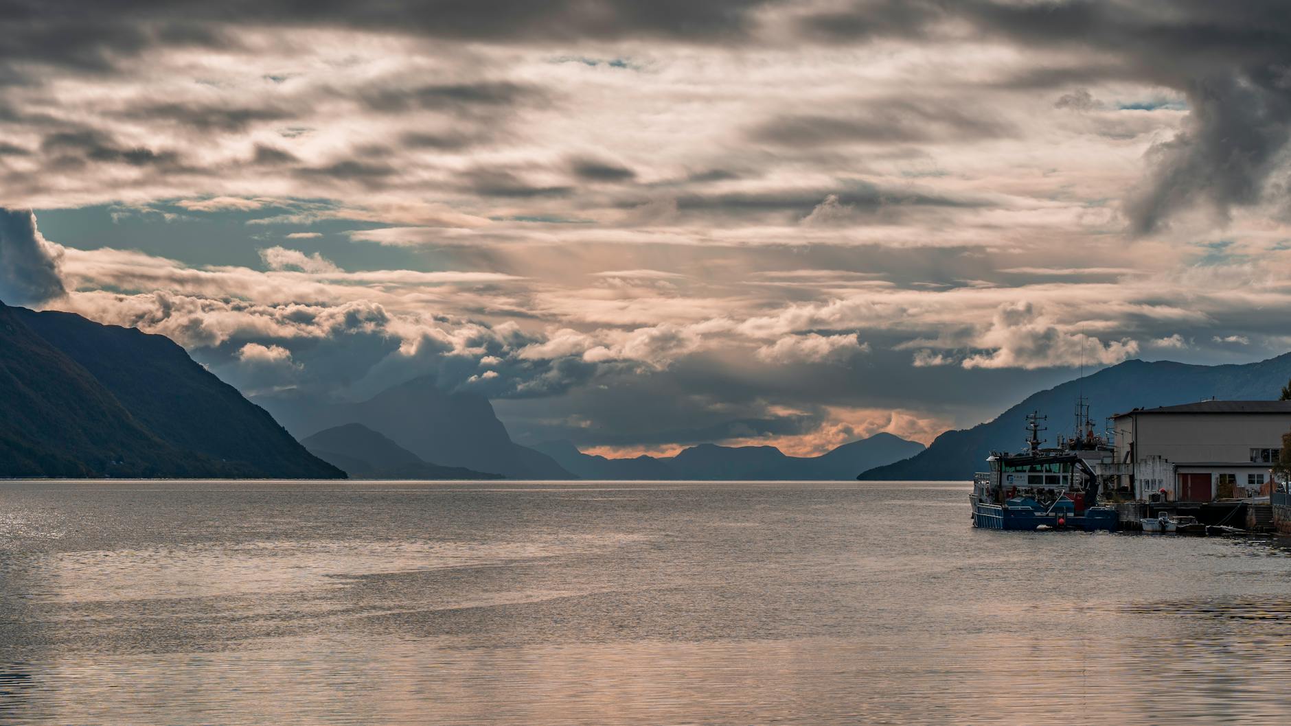 Dramatic sunset over a Norwegian fjord with cloudy skies and boats.
