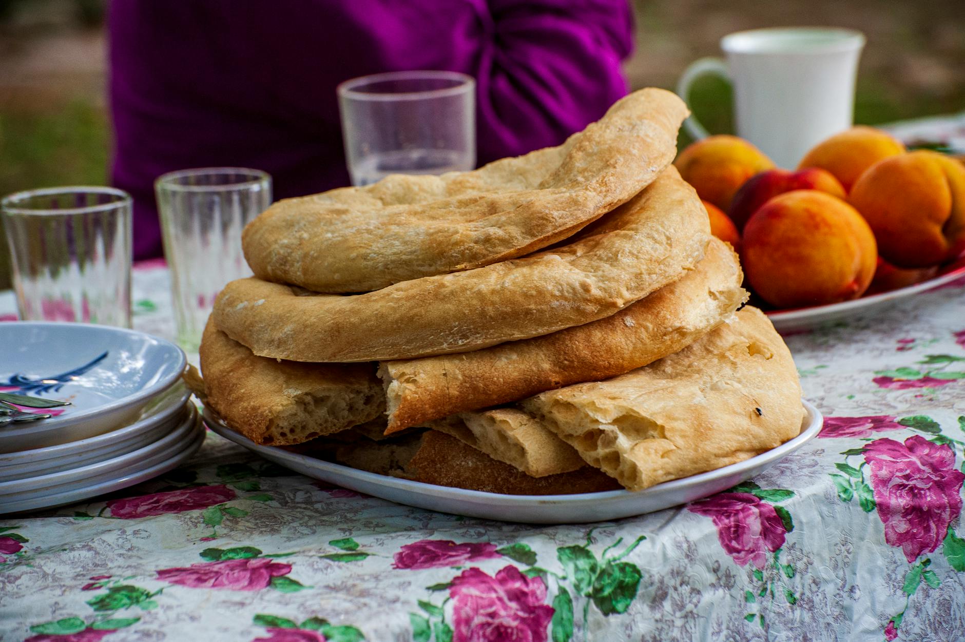 Platter of traditional Georgian bread with fresh peaches on a floral tablecloth, perfect for outdoor dining.