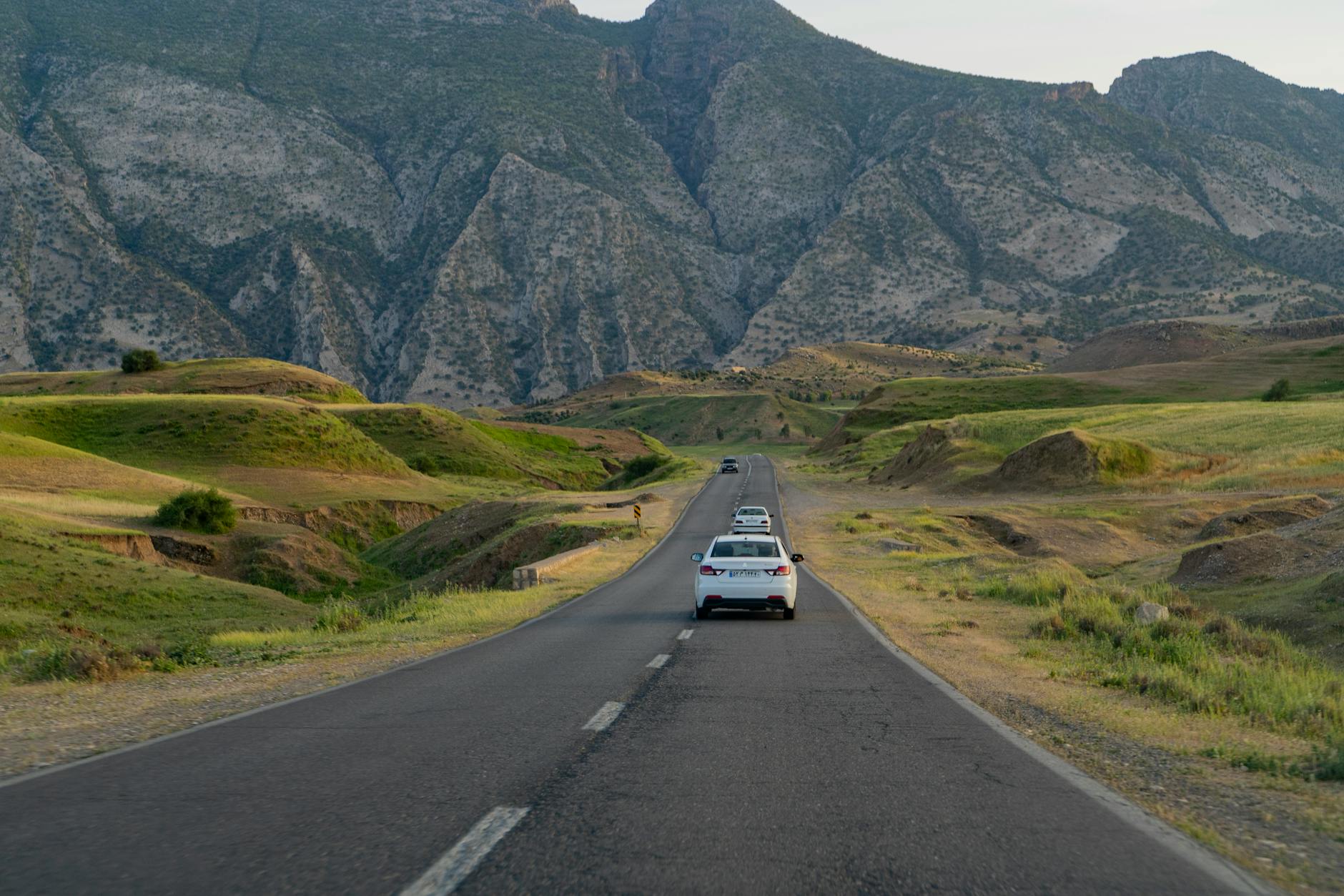 Picturesque view of a highway with cars surrounded by lush green hills and majestic mountains in summer.