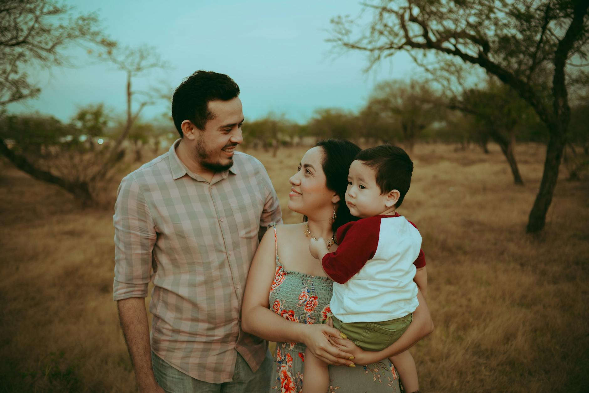Family portrait of parents with child in warm outdoors setting, capturing joyful moments together.