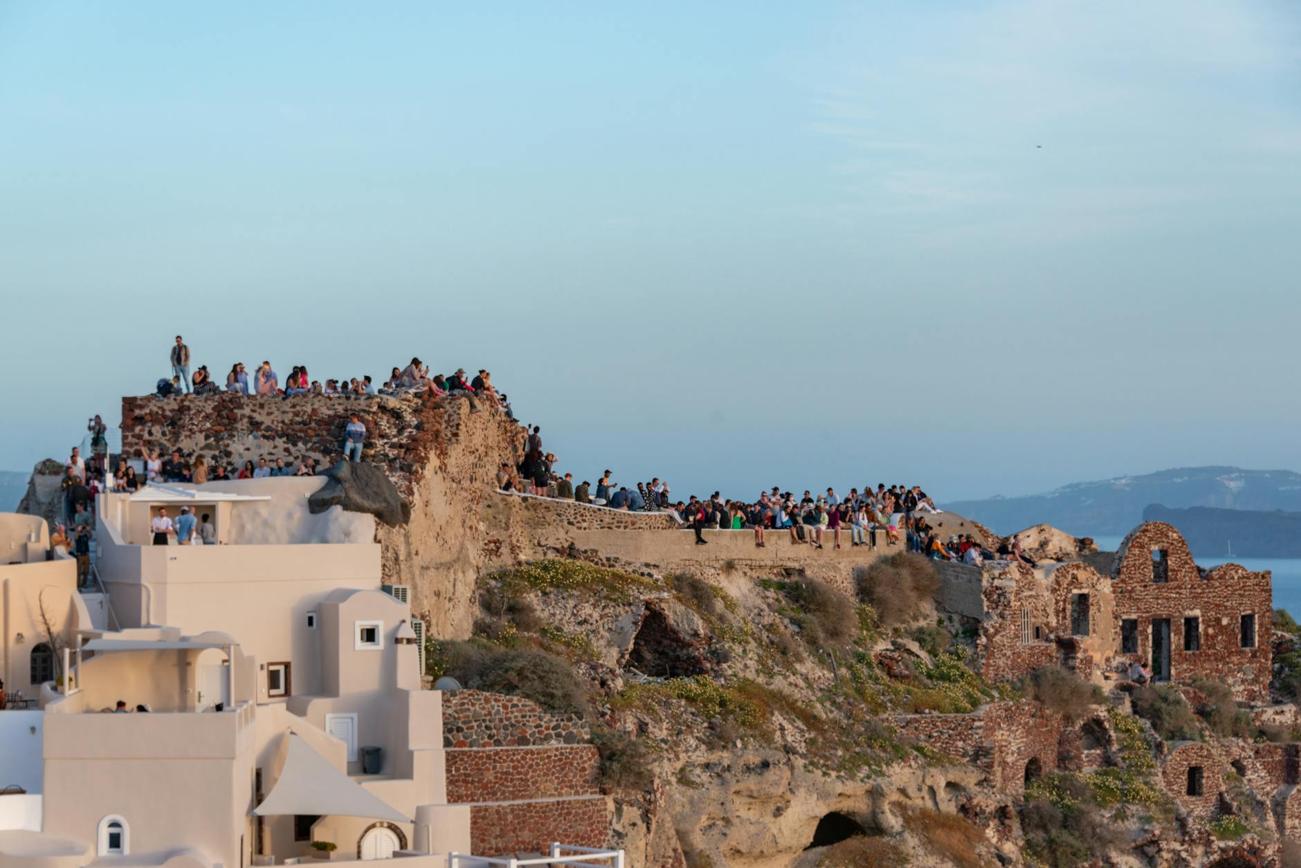A large crowd gathers on a cliff in Oia, Santorini to enjoy the breathtaking Mediterranean sunset.