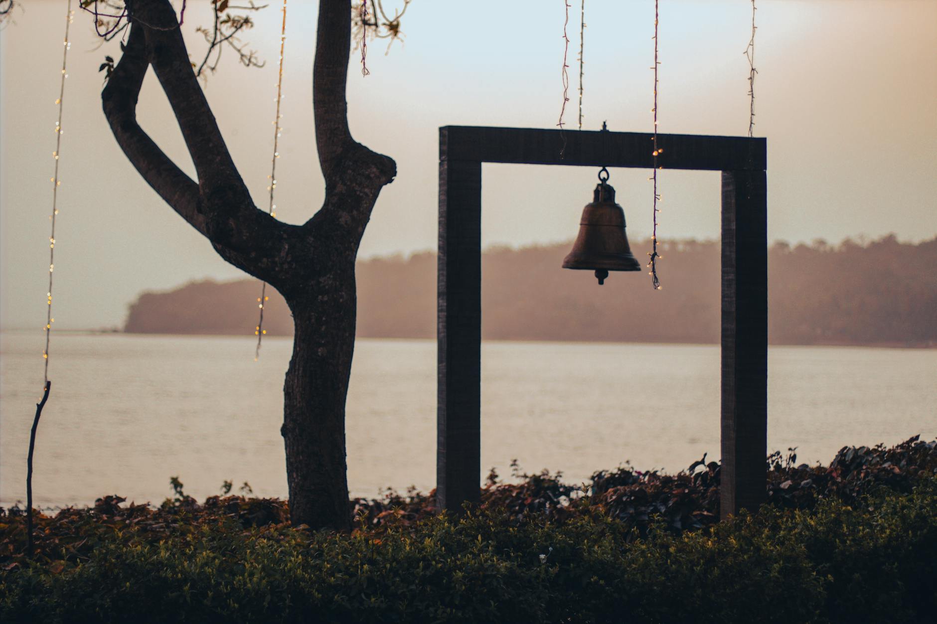 A serene view of a bell hanging against the sea and sunset in Goa, India.